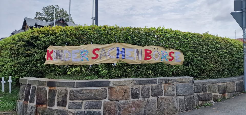 Selbstgenähtes Banner der Kindersachenbörse an einer Hecke in Wehrsdorf